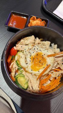 Canlı Kore Bibimbap 'ı kızarmış yumurta, tavuk, sebze ve pilav ile sıcak taş bir kasede servis edilir. Asya yemekleri promosyonları, restoran menüleri ya da mutfak blogları için mükemmel..