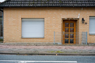 Alçak tuğlalı bir ev caddenin kenarında durur ve ön kapıdan önce kısa bir çit boşluğu kapatır, küçük bir muhafaza girişi özel ve sessiz bir çalışma altında hissettirir..