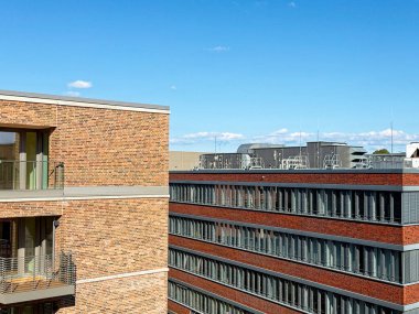 Taze taş ustası büyük bir bardakla yükselirken dört katlı sağlam bir blok kiel 'in yanında duruyor, eşleşme köşeyi etkin, dengeli ve insanların yakınlarda yaşayıp çalışabilmesi için hazır hissettiriyor..