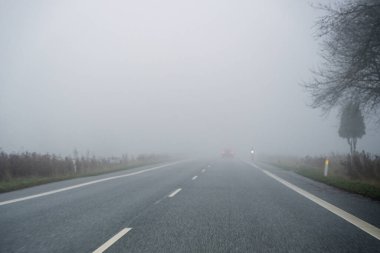 A car travels along a foggy country road with very low visibility, creating a muted atmospheric scene ideal for themes like traffic safety, weather conditions and rural transport.