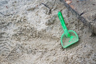 Yeşil plastik bir kürek, taştan bir kenarın yakınındaki yumuşak kumda yatar, çocukluk temaları, oyun alanları, plaj görselleri ve boş zaman kavramları için ideal basit bir açık hava sahnesi yaratır..