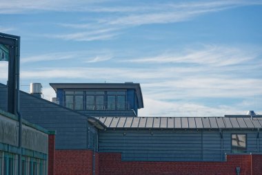 Kırmızı tuğlalı cephe, çatının üstünde sessiz bir veranda ya da gözcü odası gibi görünen bir kutu yapısı gösterir, üst katman gizlilik yeniden kullanımı ve sessiz kentsel barınak ipuçları gösterir.