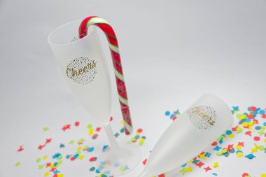 Noel neşesi ve yeni yıl kutlamalarını sembolize eden renkli konfetiler arasında, bastonlu bir şenlik kadehi duruyor. Tatil partileri, etkinlik tasarımı ve mevsimsel görseller için ideal.