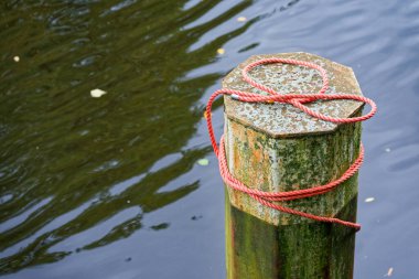 Yıpranmış kıyı demirleme direği yumuşak dalgalı suyun yanında kırmızı bir iple sarılmış. Posterler, şablonlar, seyahat tasarımları ve sakinleştirici görseller için ideal deniz ayrıntıları.