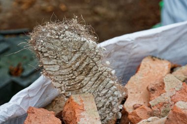 Ağır bir beton yığını, içinde hala sıkışmış metal demiri olan bir duvardan sökülmüş halde duruyor. Sivri uçlu parça, kuvvet ve hasarı gösteriyor ve yıkım çalışmalarından kalma bir hurda gibi sert zeminde duruyor..