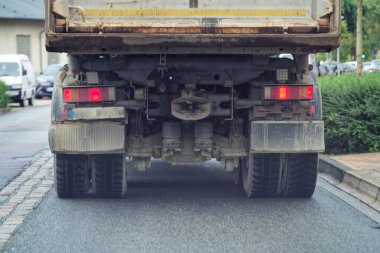 Arkadan kirli bir sanayi kamyonu gösteriliyor, ağır tekerlekleri, ışıkları ve mekanik parçaları var. Ulaşım temaları, lojistik görseller, endüstri tasarımı ve yol güvenliği konuları için ideal.