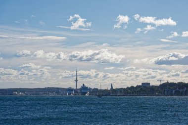 Kiel limanı yumuşak bulutların altında uzanır büyük gemiler rıhtımlar boyunca park etmiş yatların yanında dinlenirken, durgun su direkleri yansıtır ve sessiz marina sahnesi yumuşak ve neredeyse sonsuz gibi gelir..