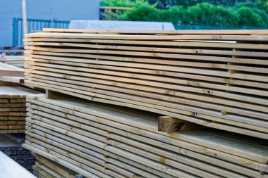 Birkaç uzun tahta yığını ahşap paletler üzerinde duruyor, soluk yüzeyler yeni bir binaya ya da projeye taşınmak için avluda düz katmanlar oluşturuyor..