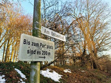 Yol tabelaları Baltık Denizi 'ni ve kışın ağaçlarla çevrili bir park alanını işaret ediyor. Bu da seyahat yönünü ve Flensburg Ostseebad kıyı turizmini simgeliyor..