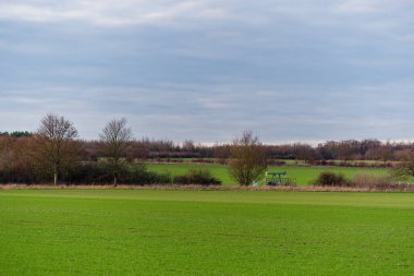 Geniş yeşil bir alan, ufuktaki küçük bir pompa Jack tarzı mekanizmasına doğru uzanır. Bu da, tarım arazisinde tek başına duran küçük bir çıkarma ya da su pompalama tesisini işaret eder..