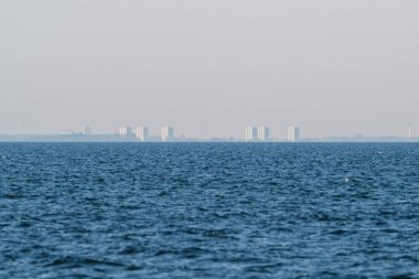 Ufukta Kopenhag 'ın soluk silueti beliriyor Koge' den göründüğü gibi sakin denizin ötesinde, uzaklığı, kentsel varlığı ve kıyı perspektifini simgeliyor.
