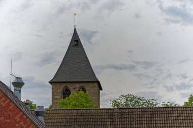 İnce bir kilise kulesi, üzerinde altın bir horoz gülü olan süslü bir kuleyle yükselir. Rüzgârla döner, sakin bir günde çatıların üzerinde parlar..