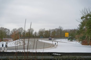 Şubat 2026 'da kar ve buzla kaplı kıvrımlı yolda kış trafiği için güvenli hava koşullarını ve Avrupa' da mevsimsel seyahat koşullarını dikkatle temsil eden araçlar kullanılıyor.