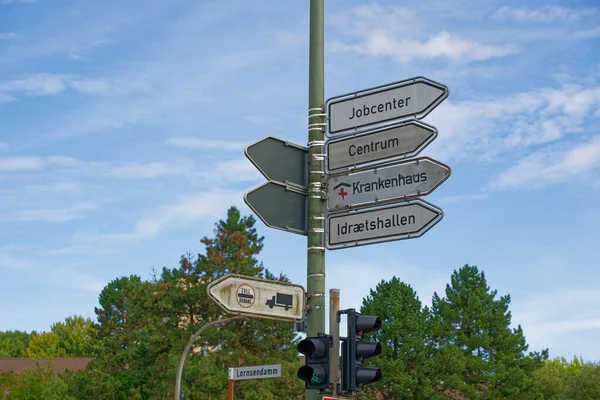 Bir kavşaktaki çoklu yön işaretleri insanları iş merkezinin spor salonlarına ve şehir merkezine yönlendiriyor. Bu da kamu hizmetlerinin ulaşılabilirliğini ve günlük şehir navigasyonunu temsil ediyor.