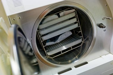 Hijyen ve güvenliği sağlamak için tıbbi ve laboratuvar araçlarını sterilize etmek için kullanılan metal tepsileri olan açık bir otoklav sterilizatörü görüntüsü.
