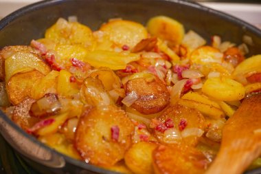 Tavada doğranmış soğan ve pastırma ile pişirilmiş kızarmış patates dilimleri. Lezzetli ve çıtır çıtır bir ev yapımı yemek sergileniyor..