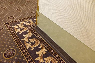 İç görünüş zengin desenli bir halı, desenli bir duvar ve sıcak tonlarda dekoratif bir süpürgeliğin yanında çiçekli ve dairesel tasarımlar içeriyor..