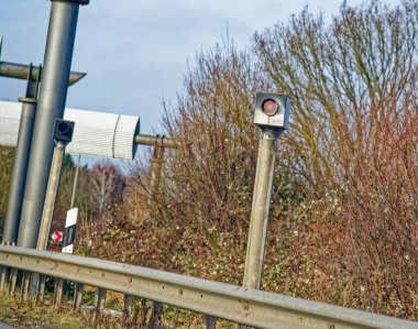 Almanya 'da trafik kameraları, arka planda bulutlu bir gökyüzünün altında bariyer ve yapraksız sonbahar ağaçları olan bir yolun yanındaki metal bir direğe monte edilmişti..