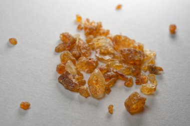 Beyaz bir zemin üzerinde sergilenen kehribar reçine kristallerinden oluşan bir koleksiyon. Şeffaf ve düzensiz şekillerini ve sıcak altın tonlarını gösteriyor..