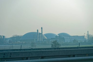 Büyük bir sanayi bölgesinde büyük yuvarlak ya da yarı yuvarlak depolama salonları ve görünür boru hatları bulunur. Ağır altyapı aktif bir sanayi bölgesinde bir fabrika veya işleme tesisi olduğunu gösteriyor..