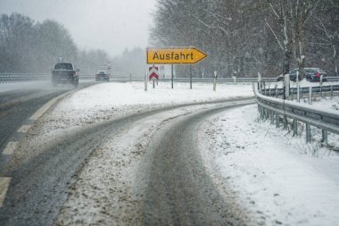 Otoban çıkış rampası kahverengi çamur ve karla kaplıdır. Ausfahrt kelimesi, sürücülere kötü kış koşullarında çıkışa doğru rehberlik ediyor..