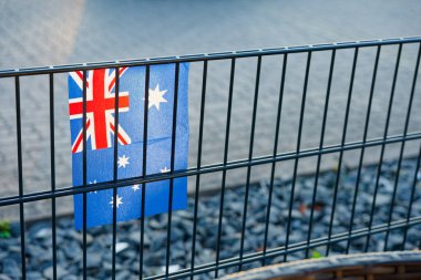 Metal bir çite sabitlenmiş Avustralya bayrağı, sınır güvenliği, göç tartışması, ulusal kimlik ve uluslararası siyaseti modern bir bağlamda temsil ediyor..