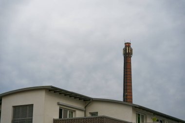 Kıvrımlı, modern çatılı beyaz bir ev merdiven ve birden fazla antenle donatılmış uzun bir direğin önünde duruyor. Karşıtlık, konut tasarımı ile araç altyapısını karıştırıyor.