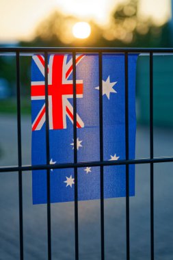 Australian flag hangs on a fence, blue field with Union Jack and white stars. The textile flutters gently, bringing bright national symbols to a public walkway.