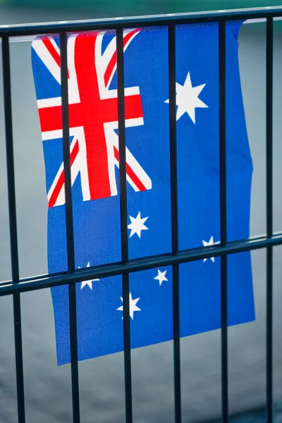 An Australian flag hangs behind black metal bars, its blue field showing the Union Jack and white stars. The small banner ripples gently in outdoor daylight.