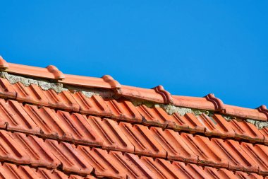 Parlak mavi gökyüzüne karşı kırmızı kil kiremitlerle kaplı bir çatı, geleneksel çatı malzemelerini ve doğal ışık dokularını sergiliyor..