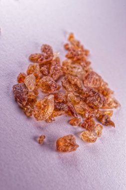 Açık bir yüzeye dağılmış doğal kahverengi şeker kristallerinin bir koleksiyonu pürüzsüz dokularını ve kehribar renklerini yumuşak ışıklandırmada sergiliyor..