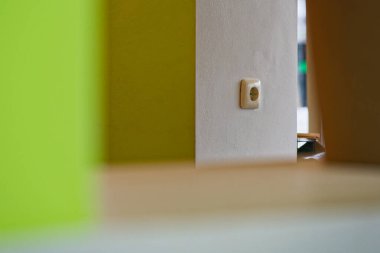 Yeşil ve beyaz renkli yüzeylerle çevrili beyaz bir elektrik prizinin yer aldığı iç duvarda, minimalist ve modern bir tasarım sergileniyor..