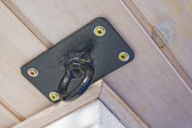 Siyah metal bir kanca, dört vida kullanılarak ahşap bir tavan paneline güvenli bir şekilde monte edilir..