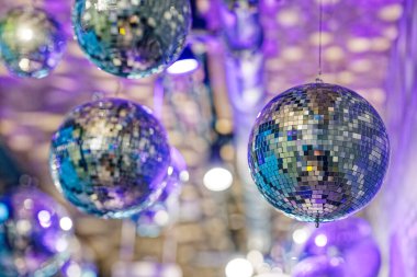 Çoklu yansıtıcı disko topları canlı mor ve mavi ışıklarla sarkıtılmış. İçerde neşeli ve canlı bir parti atmosferi yaratıyor..