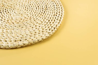 Sarı arkaplandaki kahverengi hasır masa paspasının üst görüntüsü. Saman yuvarlak tepsi, düz konum, kopyalama alanı. 