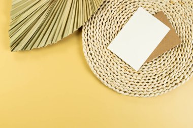 Kahverengi hasır masa paspası, sarı arka planda kurutulmuş palmiye yaprağı. Beyaz ve kahverengi kartlar, saman yuvarlak tepsi, düz döşeme, kopyalama alanı. 