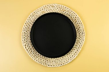 Kahverengi hasır masa paspası, sarı arka planda siyah plaka. Saman yuvarlak tepsi, düz konum, kopyalama alanı. 