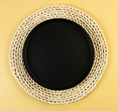 Kahverengi hasır masa paspası, sarı arka planda siyah plaka. Saman yuvarlak tepsi, düz konum, kopyalama alanı. 