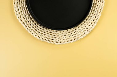 Kahverengi hasır masa paspası, sarı arka planda siyah plaka. Saman yuvarlak tepsi, düz konum, kopyalama alanı. 