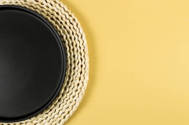 Kahverengi hasır masa paspası, sarı arka planda siyah plaka. Saman yuvarlak tepsi, düz konum, kopyalama alanı. 