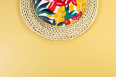 Kahverengi hasır masa paspasının üst görüntüsü, sarı arka planda renkli plaka. Saman tepsisi, egzotik bitki tabağı, yaz pikniği. Düz yat, boşluğu kopyala. 