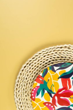 Kahverengi hasır masa paspasının üst görüntüsü, sarı arka planda renkli plaka. Saman tepsisi, egzotik bitki tabağı, yaz pikniği. Düz yat, boşluğu kopyala. 