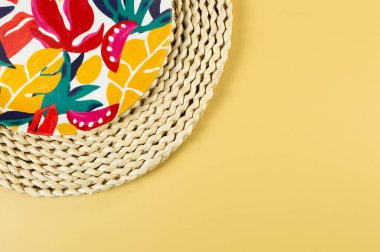 Kahverengi hasır masa paspasının üst görüntüsü, sarı arka planda renkli plaka. Saman tepsisi, egzotik bitki tabağı, yaz pikniği. Düz yat, boşluğu kopyala. 