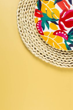 Kahverengi hasır masa paspasının üst görüntüsü, sarı arka planda renkli plaka. Saman tepsisi, egzotik bitki tabağı, yaz pikniği. Düz yat, boşluğu kopyala. 