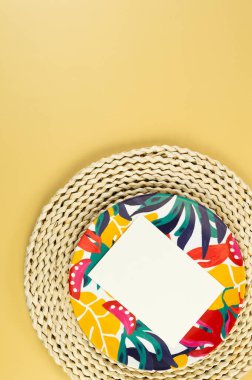 Kahverengi hasır masa paspası, beyaz kart, sarı arka planda renkli plaka. Saman tepsisi, egzotik bitki tabağı, yaz pikniği. Düz yat, boşluğu kopyala. 