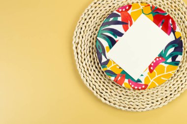 Kahverengi hasır masa paspası, beyaz kart, sarı arka planda renkli plaka. Saman tepsisi, egzotik bitki tabağı, yaz pikniği. Düz yat, boşluğu kopyala. 