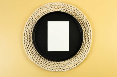 Kahverengi hasır masa paspası, siyah plaka, sarı arka planda beyaz kart. Saman yuvarlak tepsi, düz konum, kopyalama alanı. 