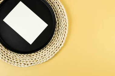 Kahverengi hasır masa paspası, siyah plaka, sarı arka planda beyaz kart. Saman yuvarlak tepsi, düz konum, kopyalama alanı. 