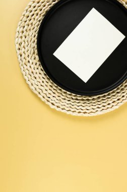 Kahverengi hasır masa paspası, siyah plaka, sarı arka planda beyaz kart. Saman yuvarlak tepsi, düz konum, kopyalama alanı. 