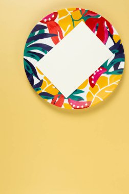 Renkli plakanın üst görüntüsü, sarı arka planda beyaz kart. Egzotik bitki plakası, yaz pikniği. Düz yat, boşluğu kopyala.